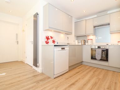 A kitchen with grey cabinets a dishwasher an oven a kettle and wooden floor at The Crest in Helston