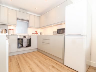 A kitchen with white cabinets a built-in oven a microwave a kettle and a refrigerator at The Crest in Helston