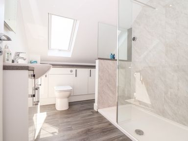 A bathroom with a toilet, sink with countertop, shower area with glass partition, storage cabinets, and a skylight window at The Crest in Helston