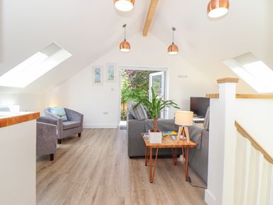 A living room with armchairs a sofa a side table with a plant and lamp and an open door to a garden at The Crest in Helston