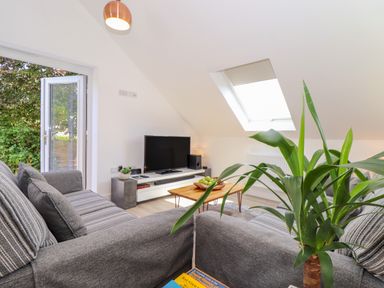 A living room with two grey sofas a wooden coffee table with fruit a television and an open door to a garden at The Crest in Helston