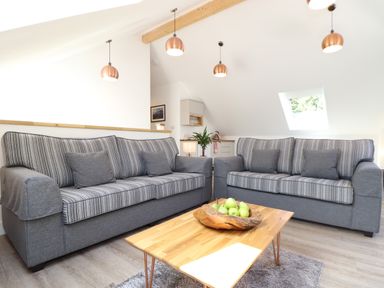 A living room with two grey sofas a wooden coffee table and hanging lights at The Crest in Helston