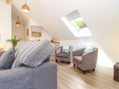 A living room with a gray sofa and two armchairs with pillows under a skylight window at The Crest in Helston