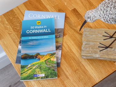 A wooden table with two Cornwall walking guidebooks and a bird sculpture on a wooden base at The Crest in Helston