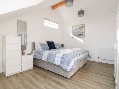 A bedroom with a bed and blue patterned bedding a tall white dresser a white nightstand with a lamp and mirror on the wall at The Crest in Helston
