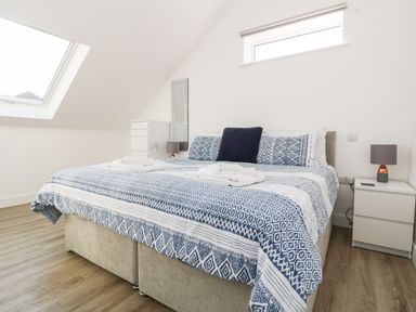 A bedroom with a bed covered in a blue and white patterned duvet beside a bedside table with a lamp and a chest of drawers at The Crest in Helston