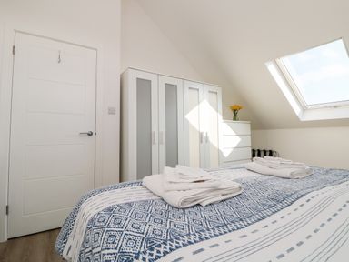 A bedroom with a bed covered with patterned blue and white bedding and folded towels on top a white wardrobe a white cabinet with a vase of flowers and a window on a slanted ceiling at The Crest in Helston