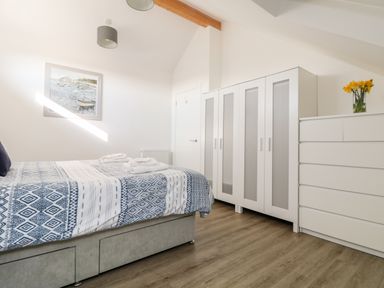 A bedroom with a bed with a patterned blue and white bedspread white wardrobes and a white chest of drawers with yellow flowers on top at The Crest in Helston