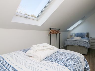 A bedroom with two single beds blue patterned bedding skylights a small clothes rack with hangers and folded towels on a bed at The Crest in Helston