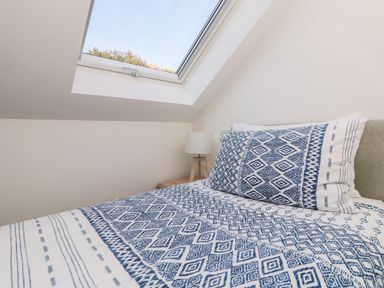 A bed with blue and white patterned bedding next to a bedside table with a lamp under a skylight at The Crest in Helston