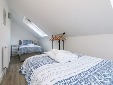A bedroom with two single beds a skylight window and a clothes rack with hangers at The Crest in Helston