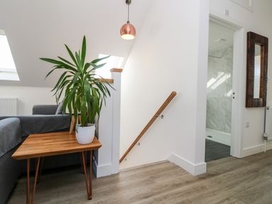 A stairway next to a wooden table with a potted plant and a gray sofa visible at The Crest in Helston