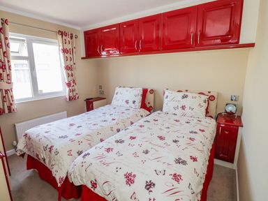 A bedroom with two single beds with patterned bedding and red cabinets above at Boosters Lodge in Stratford upon Avon