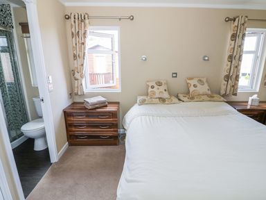 A bedroom with a double bed two windows bedside tables and an en suite bathroom at Boosters Lodge in Stratford-upon-Avon