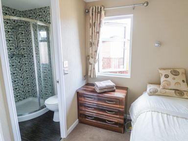 A bedroom with a bed next to a window and a chest of drawers beside an ensuite bathroom at Boosters Lodge in Stratford-upon-Avon