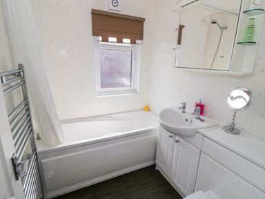 A bathroom with a bathtub shower sink mirror and towel rack at Boosters Lodge in Stratford-upon-Avon