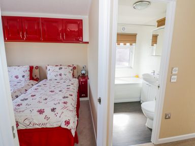 A bedroom with twin beds and red cabinets next to a bathroom with a bathtub and sink at Boosters Lodge in Stratford upon Avon