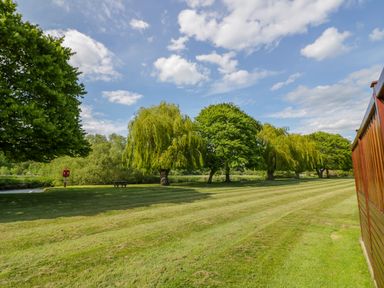 A grassy park area with trees and a bench by a river at Boosters Lodge in Stratford-upon-Avon