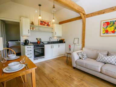 A kitchen with white cabinets wooden dining table set with bowls and glasses beige sofa with cushions wooden beams on ceiling at The Lodge at Mortons in Hankerton