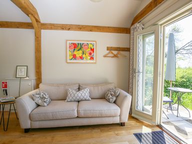A beige sofa with patterned cushions in a living room with wooden beams and a door leading outside at The Lodge at Mortons in Hankerton