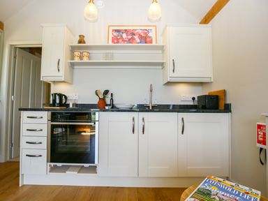 A kitchen with white cabinets a black countertop a sink an oven utensils and a magazine on a table at The Lodge at Mortons in Hankerton