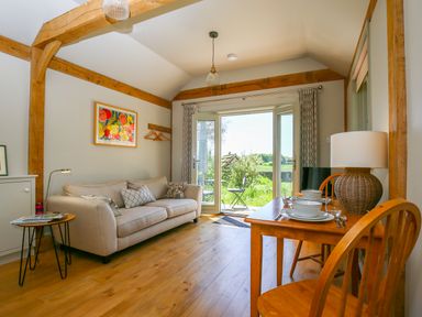 A living room with a beige sofa wooden dining table and open doors to a garden at The Lodge at Mortons in Hankerton