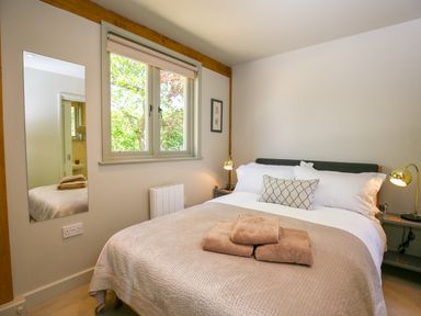A bedroom with a double bed towels on the bed side tables with lamps a window and a wall mirror at The Lodge at Mortons in Hankerton
