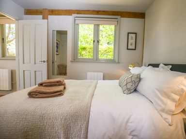 A bedroom with a bed with pillows and folded towels a window a door a mirror and a chair at The Lodge at Mortons in Hankerton