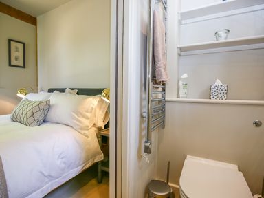 A bedroom with a bed and pillows next to a small bathroom with a toilet and shelves at The Lodge at Mortons in Hankerton