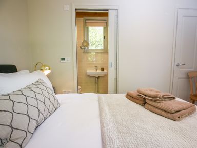 A bedroom with a bed towels on the bed a lamp on the wall and a bathroom visible through a sliding door at The Lodge at Mortons in Hankerton