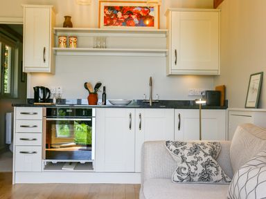 A small kitchen area with white cabinets a black countertop a kettle utensils and a sofa with patterned cushions at The Lodge at Mortons in Hankerton