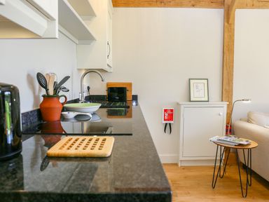 A kitchen counter with utensils and a sink next to a white cabinet with a framed picture and a small wooden table with magazines at The Lodge at Mortons in Hankerton