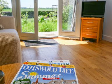 A living room with a wooden floor sofa magazine on table glass doors opening to garden and wooden TV stand with television at The Lodge at Mortons in Hankerton