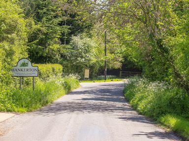 A country road surrounded by trees and greenery with a Hankerton sign at The Lodge at Mortons in Hankerton