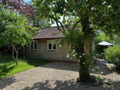 A cottage with trees and a patio area at The Lodge at Mortons in Hankerton
