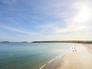 A beach with a few people walking along the shore and islands in the distance at Pen Y Garth in Mynytho near Llanbedrog