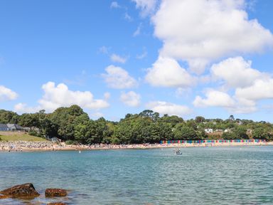 A beach with people and colorful beach huts along the shore with trees and houses in the background at Pen Y Garth in Mynytho near Llanbedrog