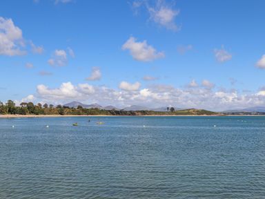 A coastal landscape with calm water boats and hills in the distance at Pen Y Garth in Mynytho near Llanbedrog