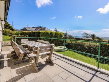 A patio with a wooden table and benches at Pen Y Garth Mynytho near Llanbedrog