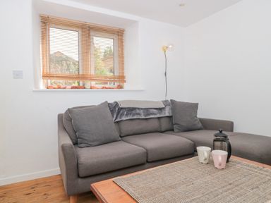 A gray sofa with cushions and a throw blanket beside a window with wooden blinds and a wooden coffee table with cups and a French press at Abbey Cottage Montacute