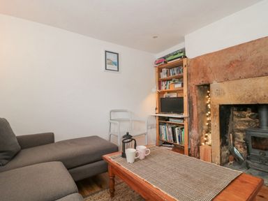 A living room with a gray sofa white chair wooden bookshelf and stone fireplace at Abbey Cottage Montacute