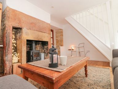 A living room with a stone fireplace wooden coffee table and a chair under the stairs at Abbey Cottage Montacute