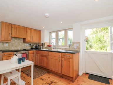 A kitchen with wooden cabinets black countertops and a white door leading outside at Abbey Cottage Montacute