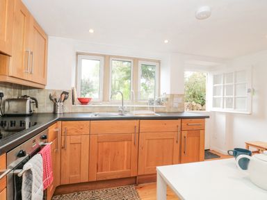 A kitchen with wooden cabinets a black countertop and a white table at Abbey Cottage Montacute Montacute