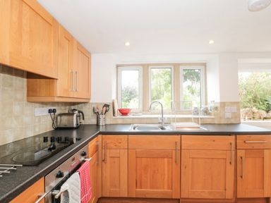 A kitchen with wooden cabinets black countertop a sink toaster and oven at Abbey Cottage Montacute