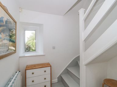 A small stairway area with white stairs a wooden chest of drawers a window and a framed picture on the wall at Abbey Cottage Montacute