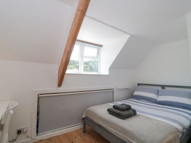 A bedroom with a striped bedspread and folded towels on the bed near a window with a wooden beam at Abbey Cottage Montacute