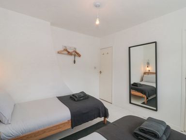 A bedroom with two single beds a wall mirror and hangers on the wall at Abbey Cottage Montacute