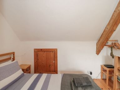 A bedroom with a bed striped bedding folded towels bedside tables wooden beam and a small wooden storage door at Abbey Cottage Montacute