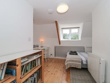 A bedroom with a single bed, desk with chair, bookshelf, and window showing trees at Abbey Cottage Montacute